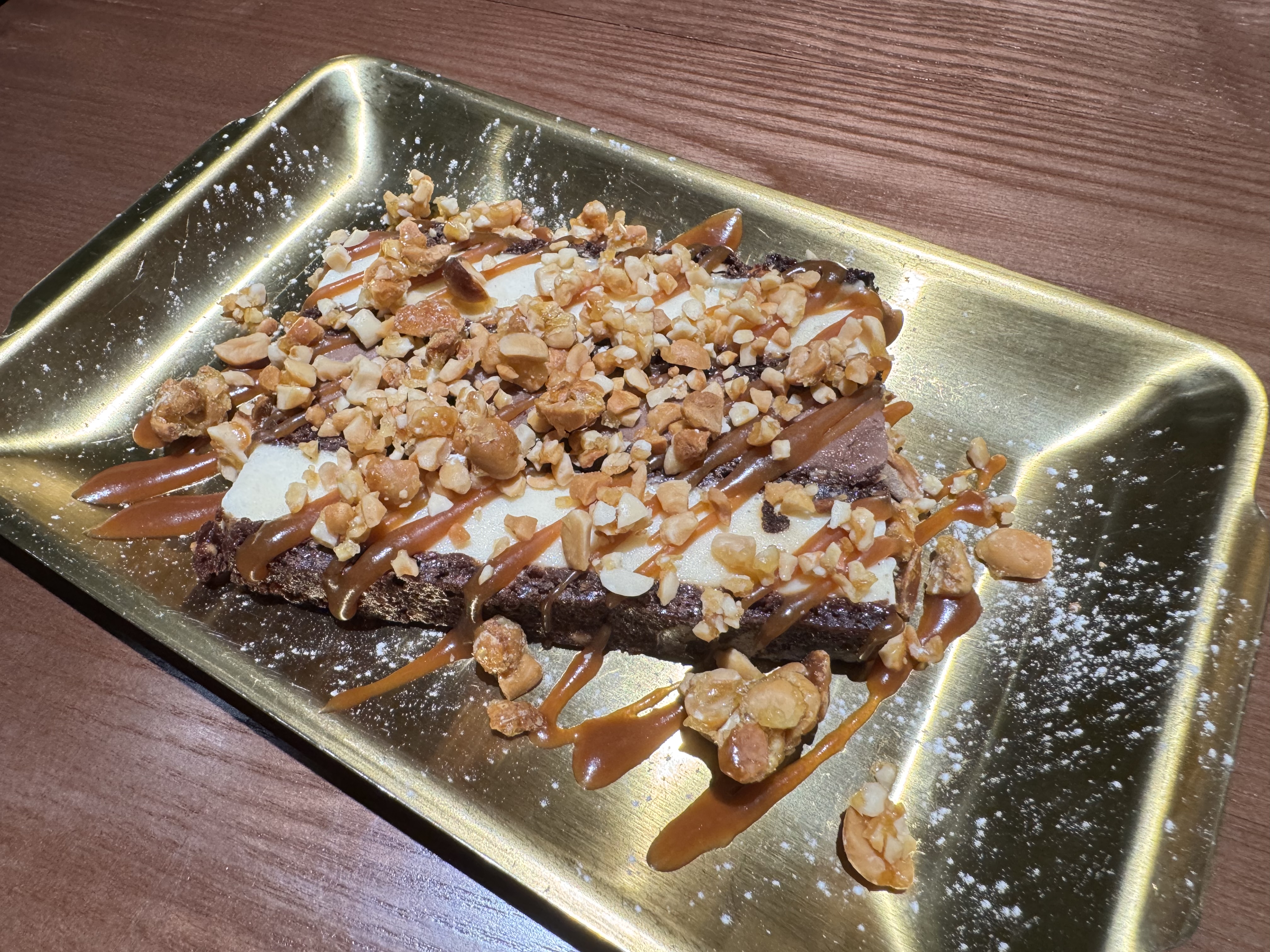 Món tráng miệng phủ caramel, hạt rang và đường bột trên khay kim loại